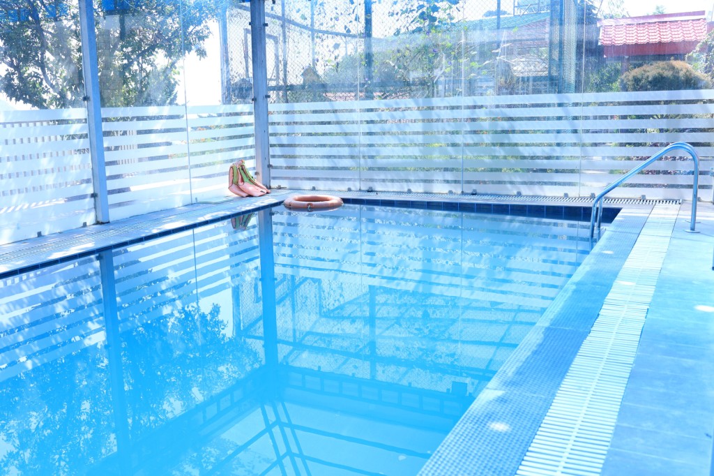 Clean outdoor swimming pool with glass safety fencing and metal ladder at Shivalaya Resort by botanix